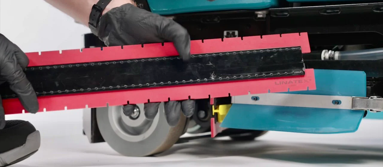 Hands removing a floor scrubber squeegee for routine maintenance