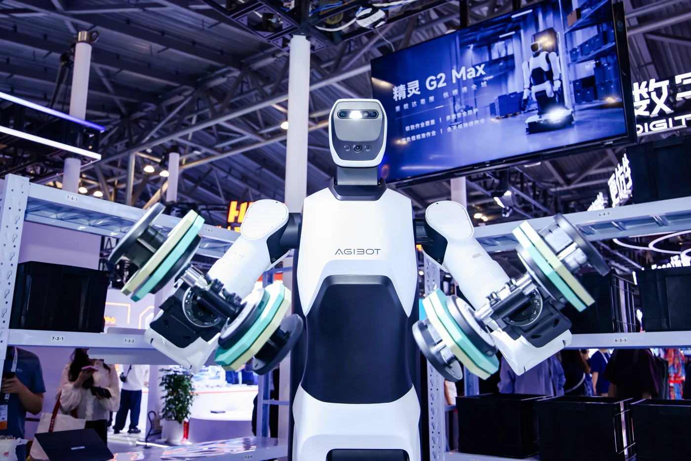 G2 Max at an exhibition holding several devices, with model signage behind it.