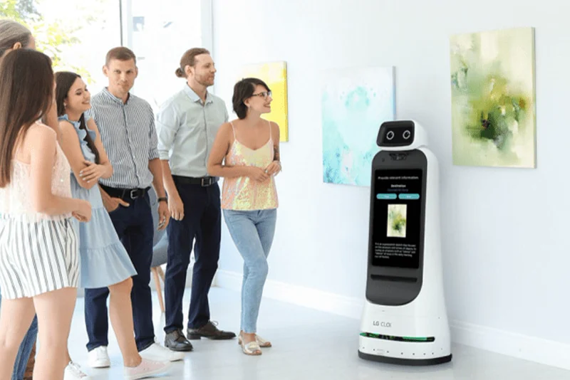 روبوت GuideBot يقود مجموعة صغيرة في معرض فني، مع معلومات الأعمال على شاشة جسمه.